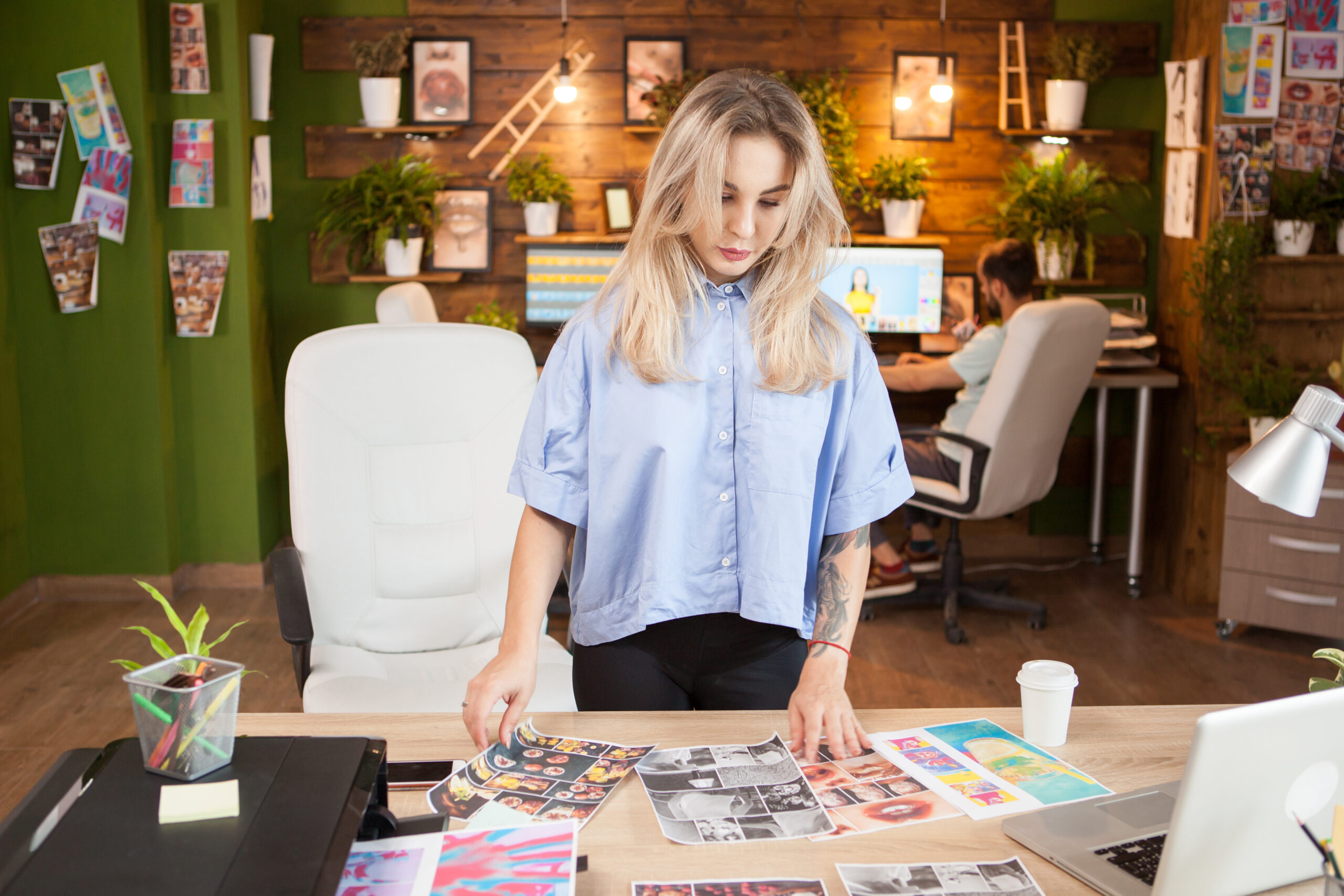 Young woman reviewing print-on-demand designs at desk with laptop and printed samples.