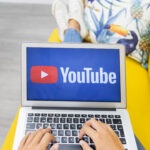 Female hands typing on laptop keyboard while working on a YouTube channel setup at home