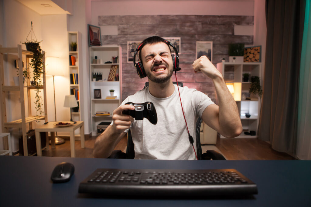 Young gamer celebrating a win while playing an online shooter game with a wireless controller