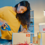 Young Asian woman packing products for an online order at her home-based eCommerce business during nighttime.