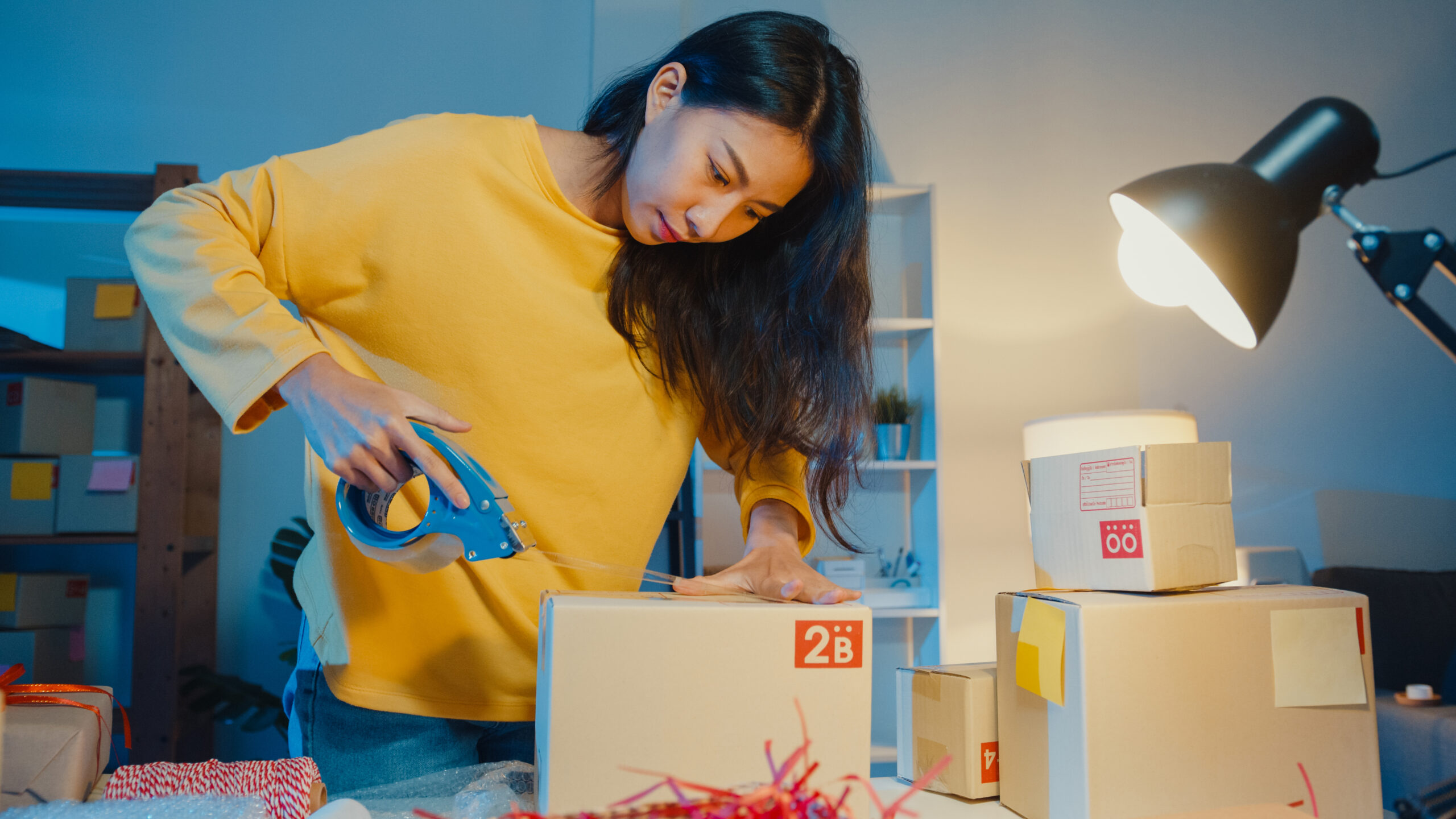 Young Asian woman packing products for an online order at her home-based eCommerce business during nighttime.
