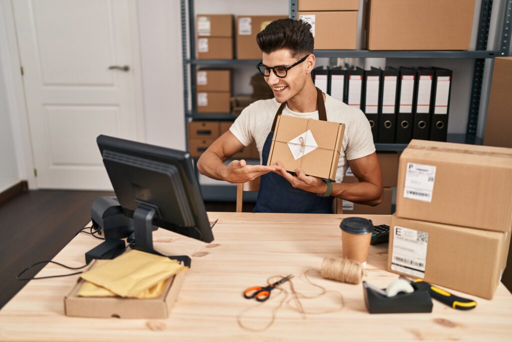 Young Hispanic eCommerce entrepreneur showing a product package during a video call from his office workspace.